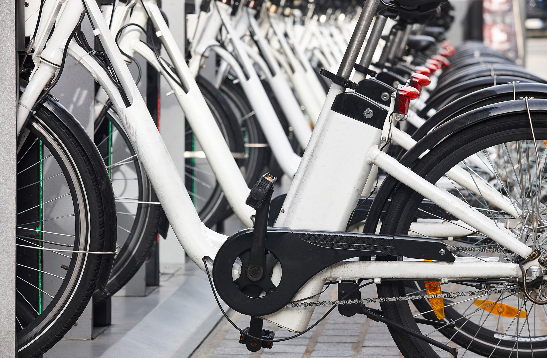 A row of white electric bicycles is parked closely together at a bike-sharing station, with their wheels aligned and secured in place.